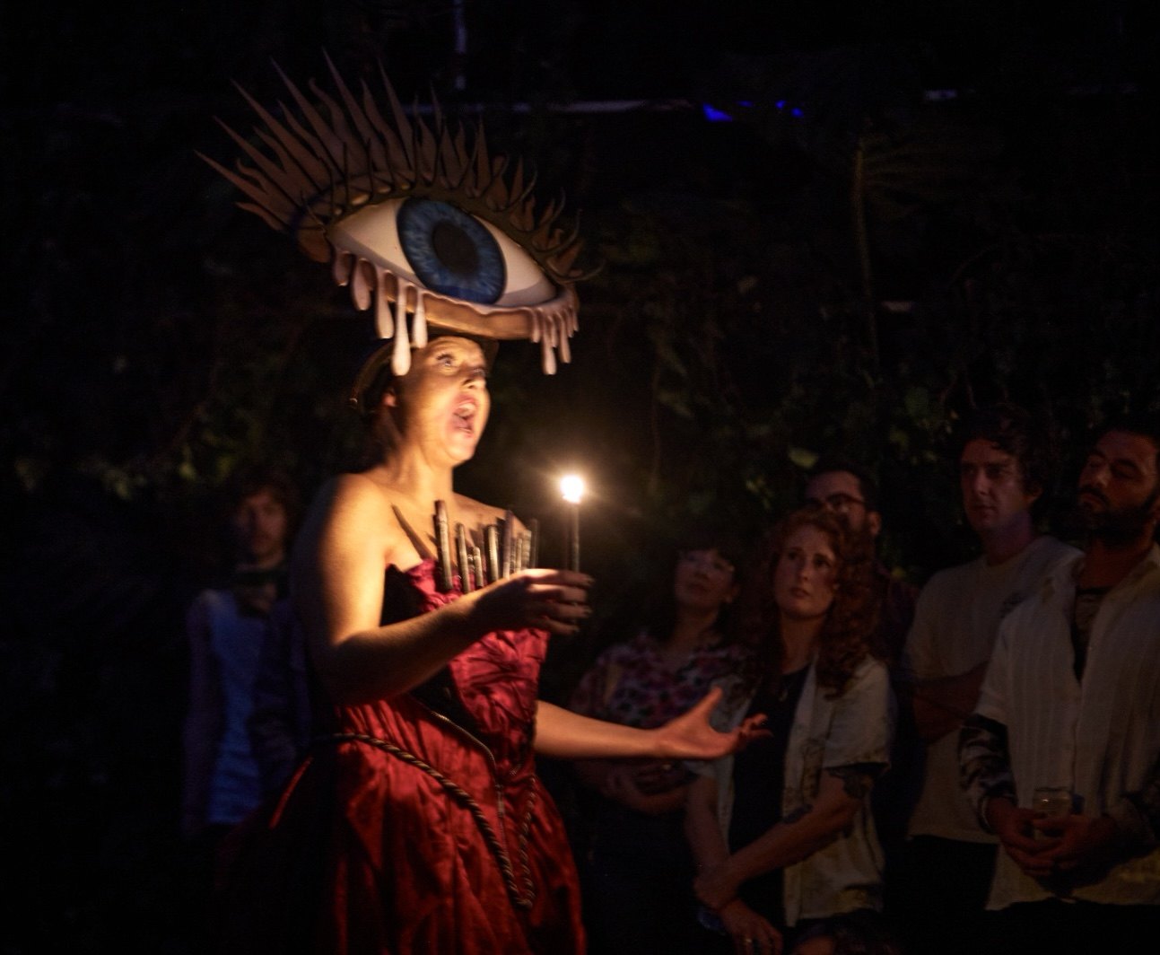 Laura King singing by candlelight among the audience, in the eye headdress.
