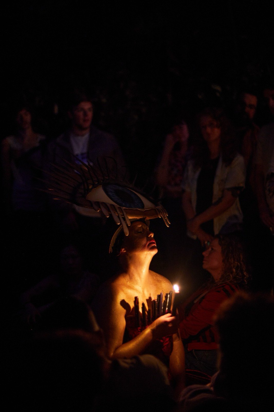 Laura King in profile, lit by a single candle, the audience around her in the dark.